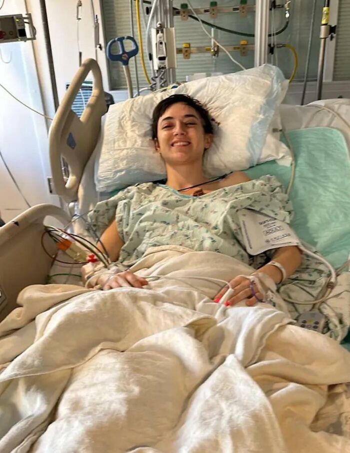 Young person in a hospital bed smiling, connected to medical equipment, showing amazing luck in recovery.