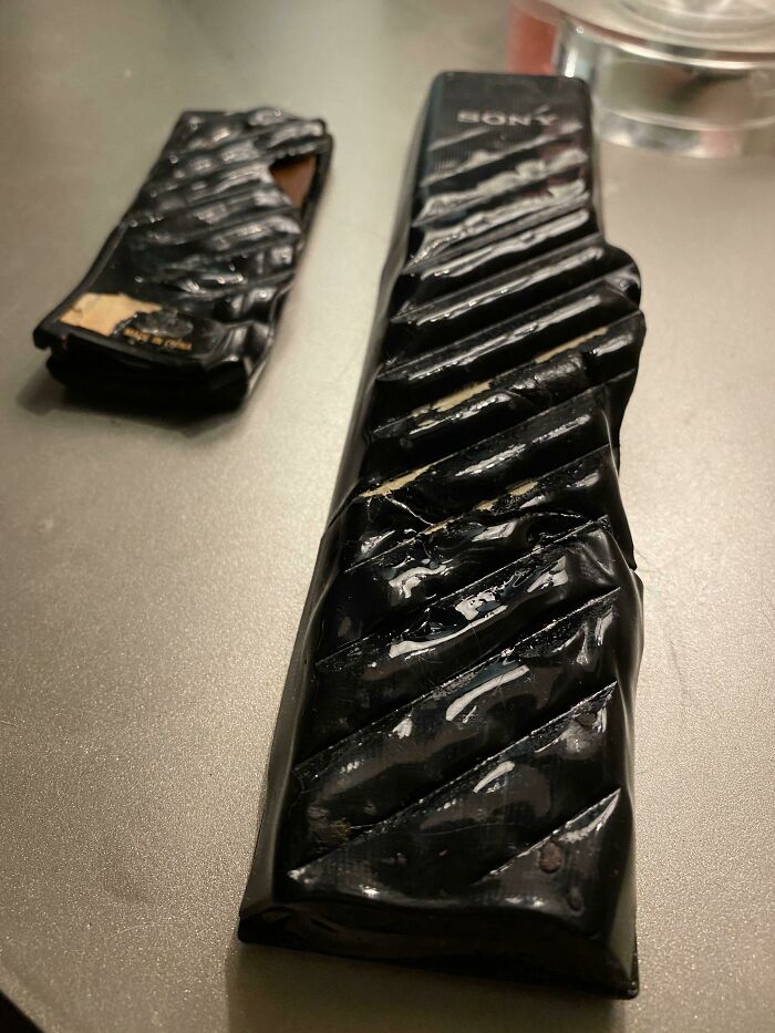 Melted black Sony remote and broken part on table, showing funny unfortunate situations of forgetting something.