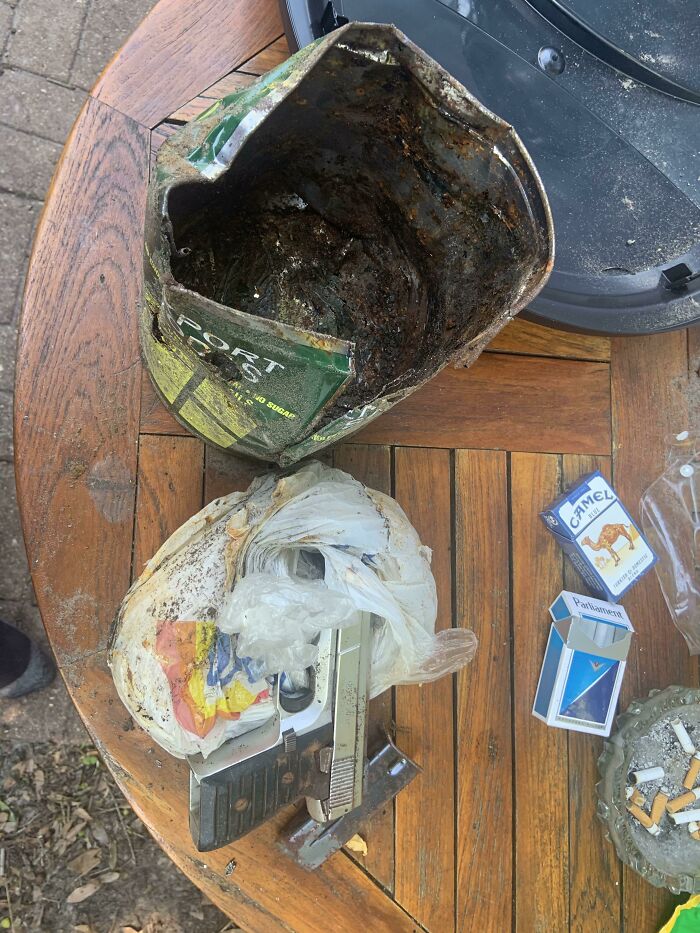 Rusty old items including a crushed can, plastic bag, and metal objects found under floorboards in an old home.