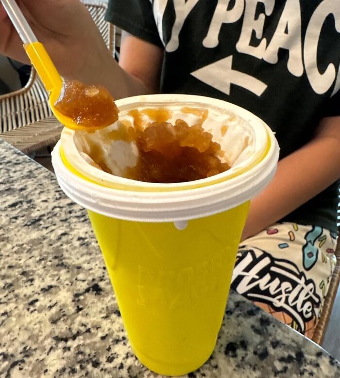 Person holding spoon with ice-filled yellow cup, demonstrating heatwave hacks for keeping cool during summer.