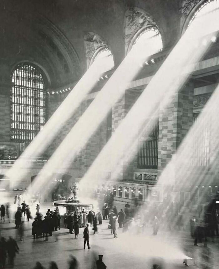 Sunbeams streaming through large windows in old architecture interior filled with people, showcasing historical building beauty.