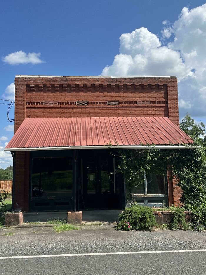 Old brick building with red metal roof and green ivy, showcasing beautiful old things in a rural setting on a sunny day