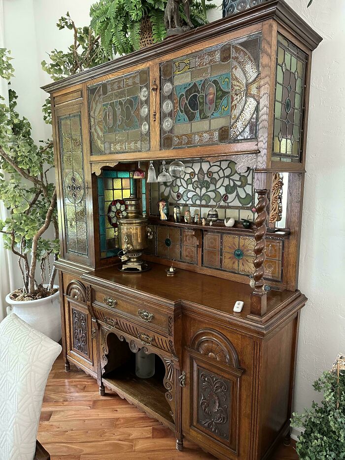 Antique wooden cabinet with intricate stained glass panels and decorative carvings in a cozy home setting.