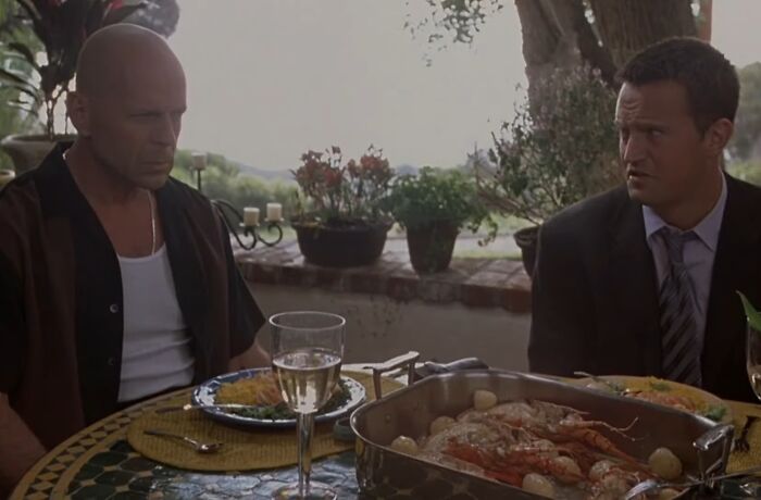 Two men sitting at an outdoor table with food and wine, from one of the worst movie sequels cinematic crimes.