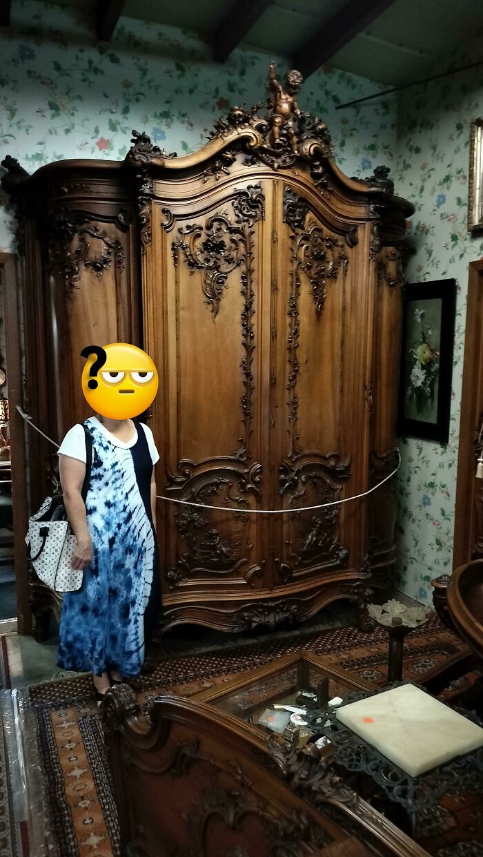 Woman standing beside an intricately carved antique wooden wardrobe, showcasing beautiful old things in a vintage room setting