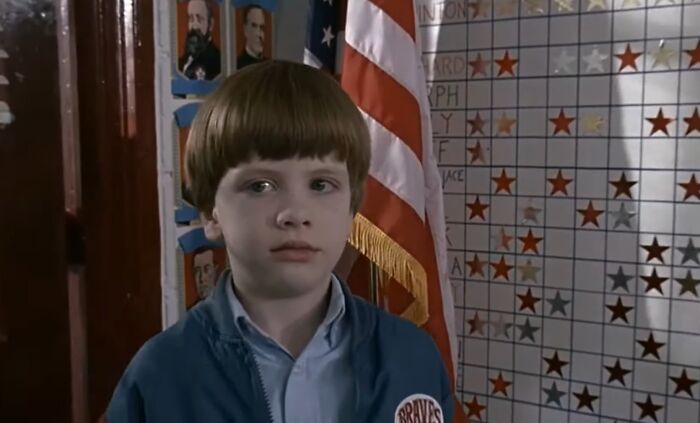 Young boy in front of an American flag and reward chart, a scene from cinematic crimes in movie sequels.