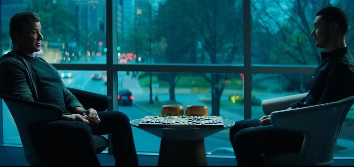 Two men sitting across from each other at a table in a dimly lit room, evoking cinematic crimes and movie sequels.
