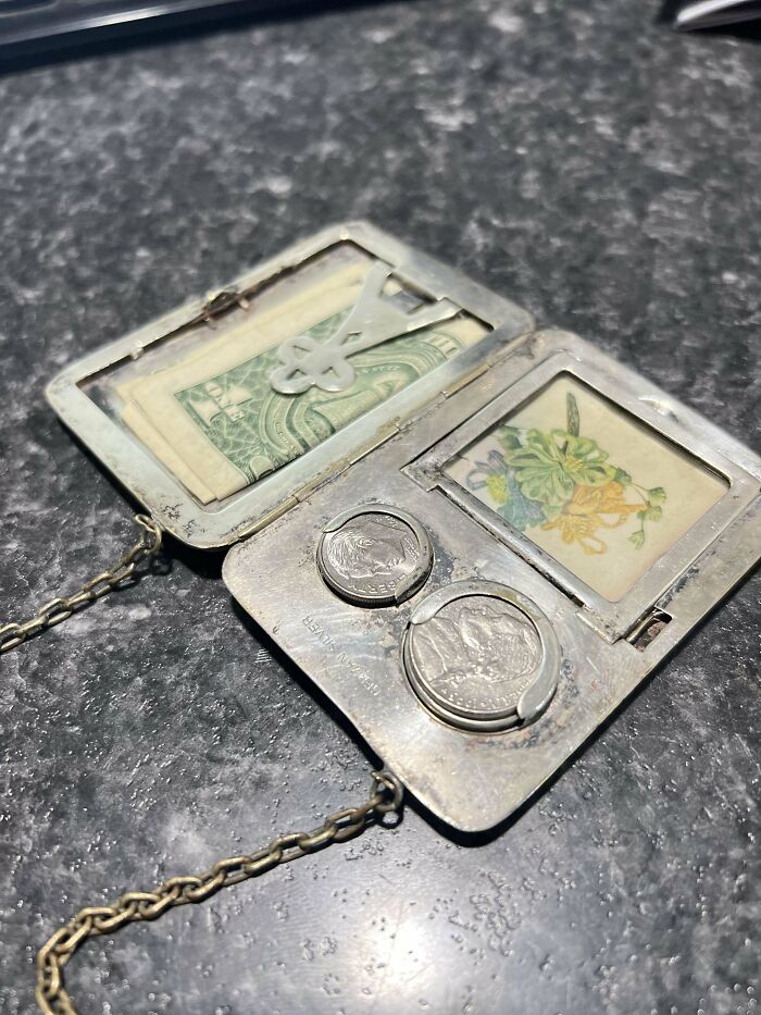 Vintage silver money clip with old coins, a dollar bill, and a floral card on a dark textured surface, showcasing beautiful old things.