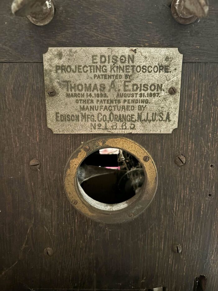 Close-up of a beautiful old Edison projecting kinetoscope with a worn metal label on aged wooden surface.