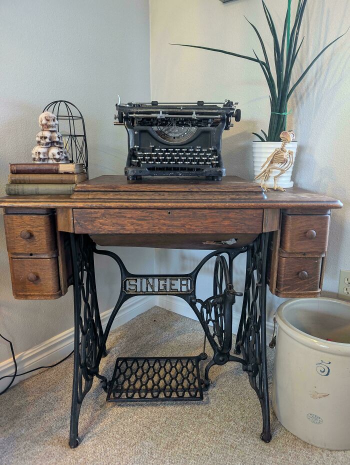 Vintage Singer sewing machine table with an old typewriter, antique books, and decorative skull and bird skeleton ornaments.