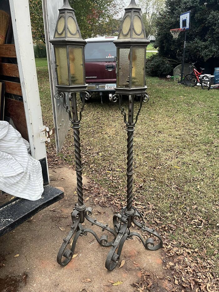 Pair of beautiful old vintage wrought iron lantern stands with twisted bases and amber glass panels outdoors on grass.