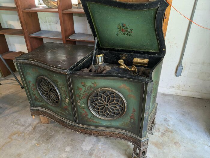 Antique green wooden phonograph with ornate floral designs and metal speaker grills standing on carved legs.