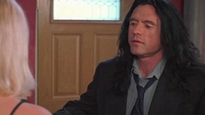 Scene from one of the worst movies of all time featuring a man with long dark hair inside a house near a blonde woman.