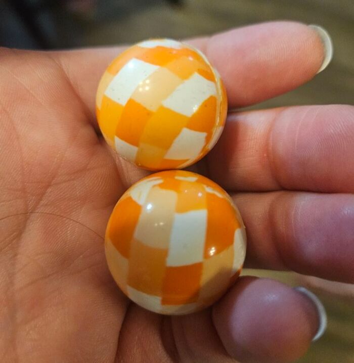 Hand holding two small orange and white checkered balls, showing a real-life glitch in the matrix phenomenon.