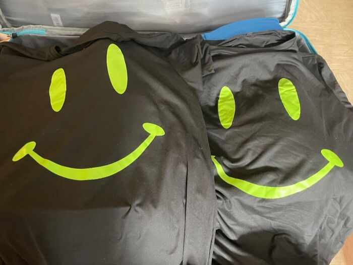Two identical black shirts with bright green smiley face designs, illustrating real-life glitches in the matrix.