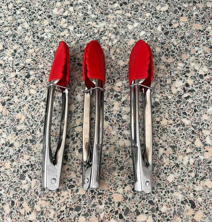 Three metal kitchen tongs with red silicone tips arranged on a speckled countertop showing real-life glitches in the matrix.