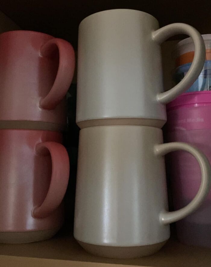 Two beige mugs stacked upside down showing a real-life glitch in the matrix with mismatched handles on a shelf.