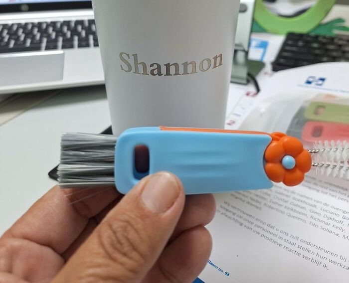 Small cleaning brush with flower handle held near a personalized cup, showcasing random things surprisingly useful.
