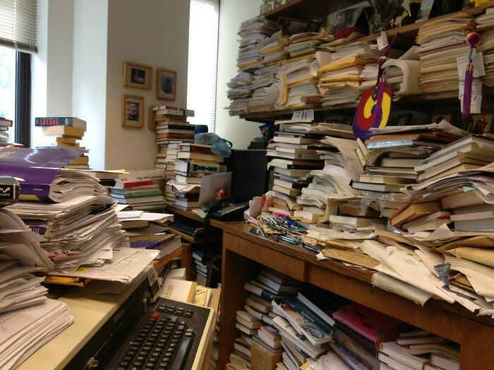 Cluttered room with stacks of papers and books showing a suspiciously unbothered disregard for organization.