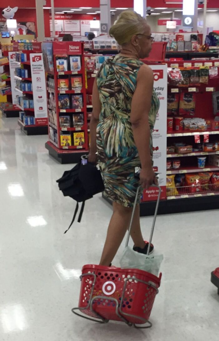 Woman at a store carrying a basket on the floor with one foot inside, showing suspiciously unbothered attitude.