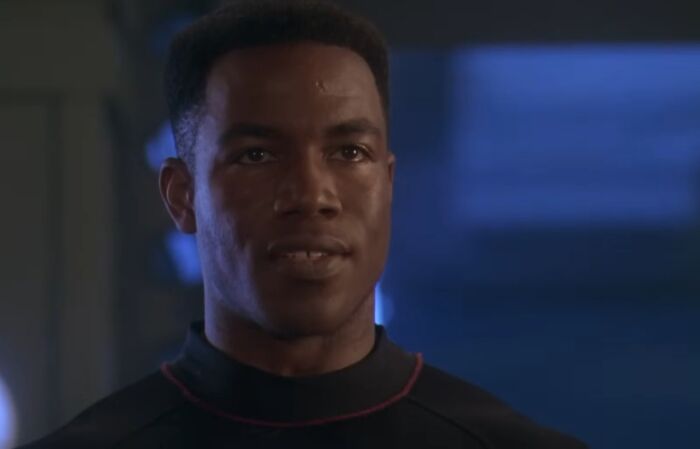 Young man in a dark outfit with a serious expression in a dimly lit scene from cinematic crimes movie sequels.