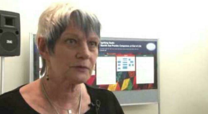 Elderly woman with short hair speaking in front of a display board showcasing unusual and cool world facts.
