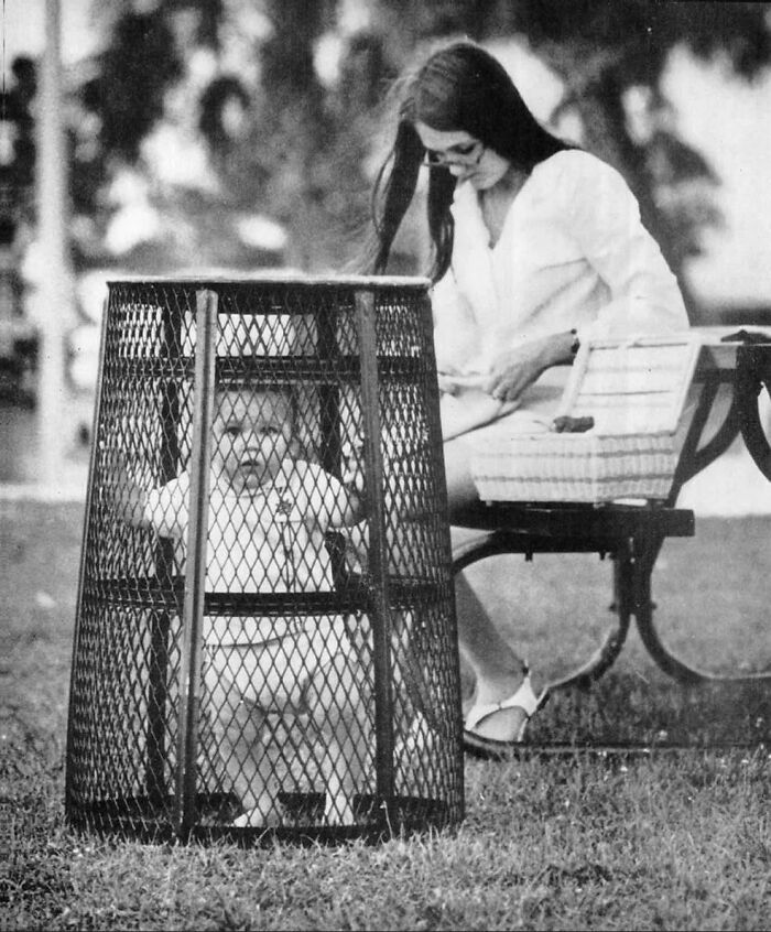 Black and white photo of a baby inside a large cage-like enclosure with a woman sitting on a bench nearby unusual world facts