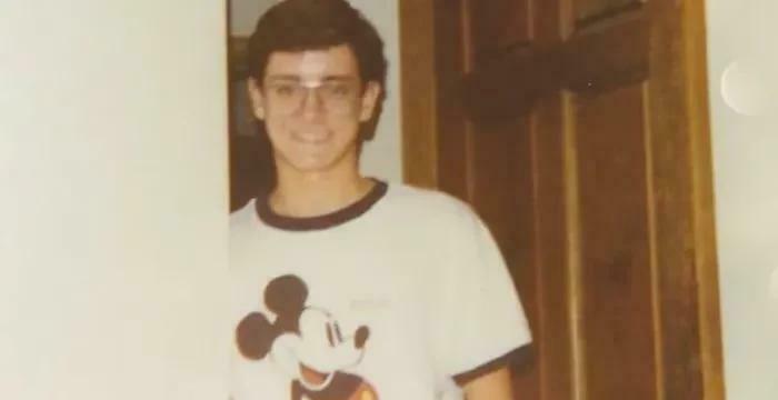 Young man wearing glasses and a Mickey Mouse shirt smiling indoors, representing unusual and cool world facts.