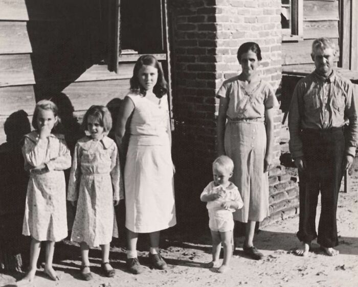 Family standing barefoot outside their home during the Great Depression era, showing daily life in a rare photo.