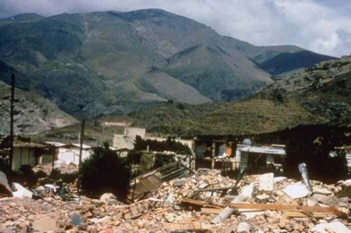 Widespread destruction from a natural disaster in a mountainous area showing rubble and damaged buildings.