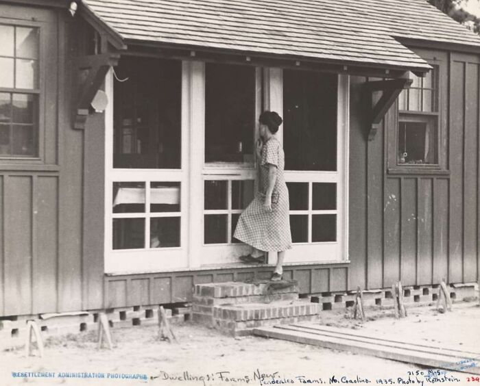 Woman in a checkered dress standing on steps outside a wooden house during the Great Depression era rare photo.