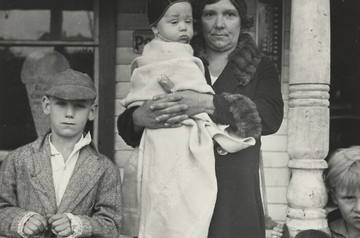 Woman holding a child with two boys standing beside her on a porch, rare photo from the Great Depression era.