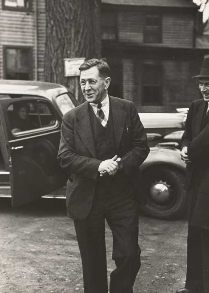 Man in suit and glasses standing by a vintage car, captured in a rare photo from the Great Depression era.