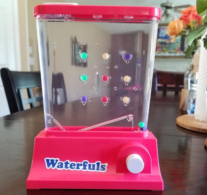 Retro Waterfuls handheld water puzzle toy with colorful pegs on a wooden table in a home setting