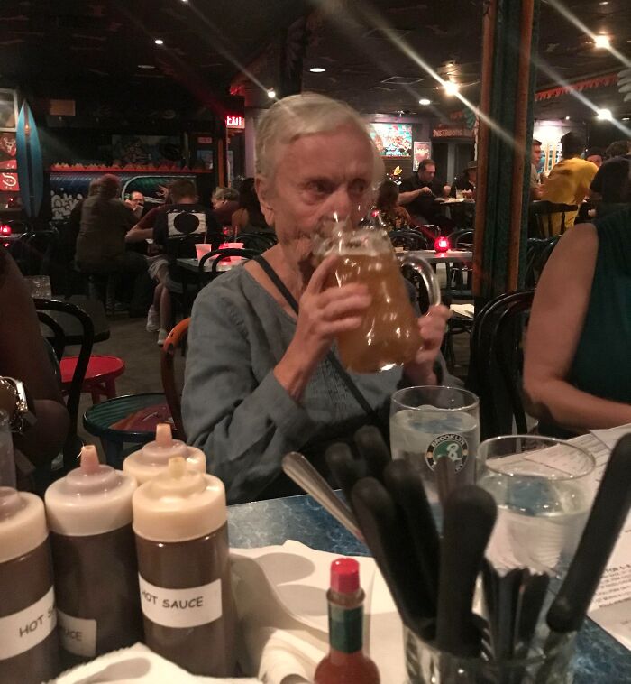 Older woman drinking beer in a busy bar, displaying a suspiciously unbothered attitude toward her surroundings.