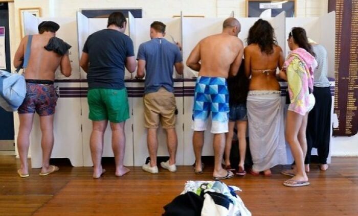 People standing casually at voting booths showing a suspiciously unbothered attitude in a relaxed environment.