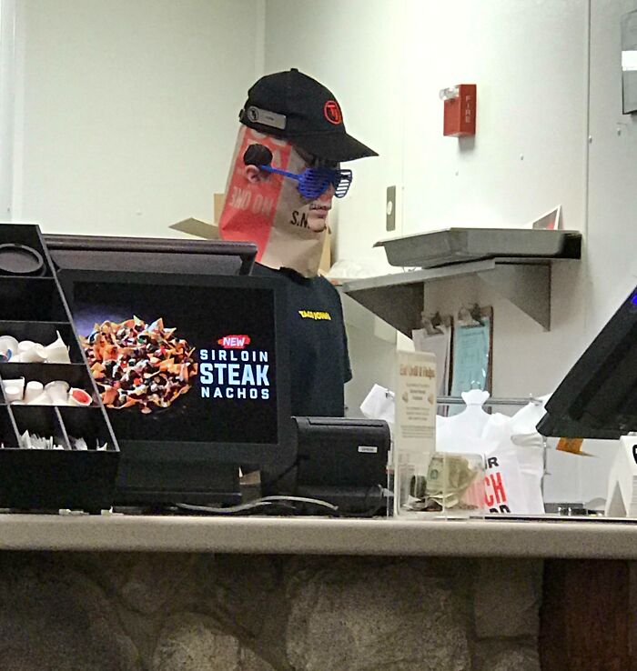 Fast food worker wearing sunglasses and a paper bag on their head, showing suspiciously unbothered attitude at work.