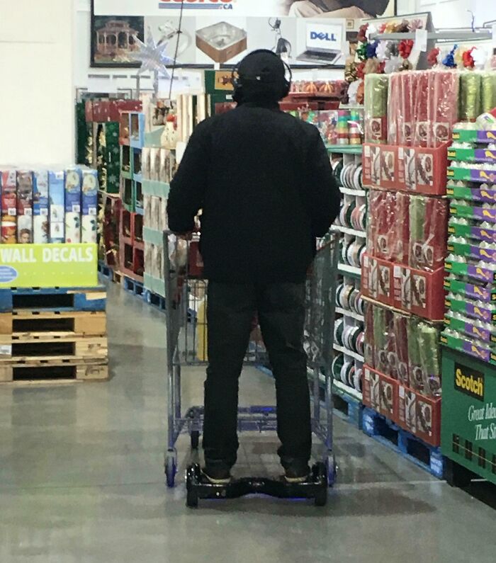Person riding a hoverboard while pushing a shopping cart in a store aisle, showing suspiciously unbothered attitude.