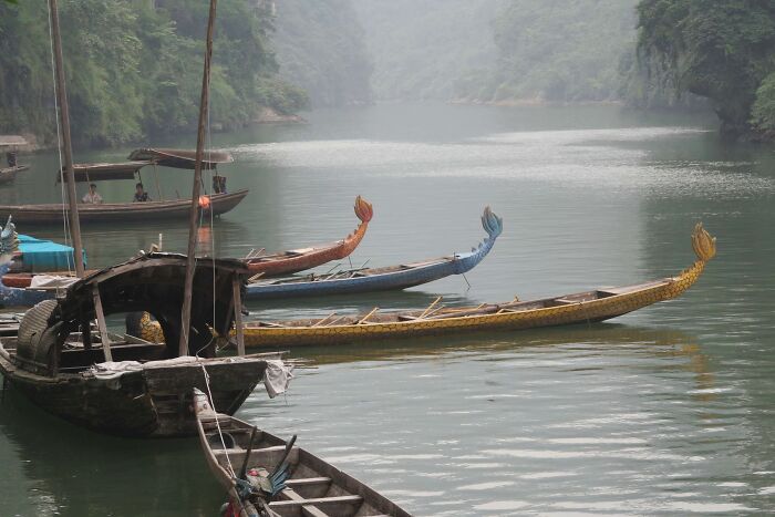 Traditional wooden boats resting on calm river water surrounded by misty forest, symbolizing natural disasters' impact.