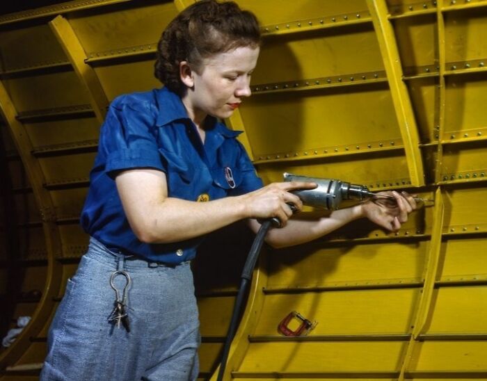 Woman at work during WWII using a power drill inside aircraft structure, showcasing bold and brilliant women at work.