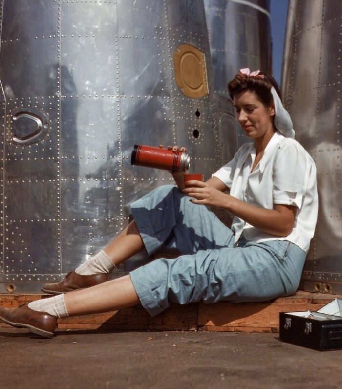 Woman at work during WWII sitting by airplane, pouring a drink from a thermos, representing women at work during WWII.
