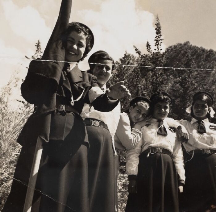 Group of women in vintage uniforms smiling outdoors in a black and white photo capturing daily life in the 50s.
