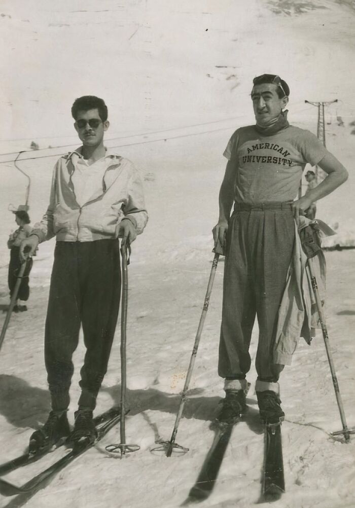 Two men skiing on snowy slopes, dressed in 1950s attire, capturing daily life across the globe in the 50s.