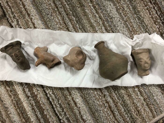 Ancient pottery and figurines laid on white cloth, resembling fossil discoveries found under old floor boards in homes.