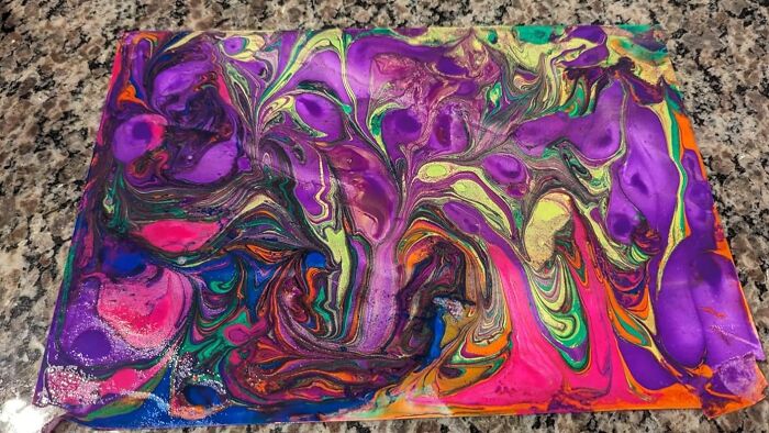 Colorful abstract marbled gift wrap with vibrant purples, greens, pinks, and oranges on a granite countertop surface.