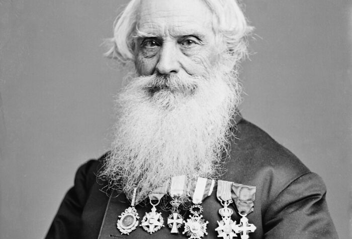 Black and white portrait of an elderly man with a long white beard wearing multiple medals showcasing unusual world facts.