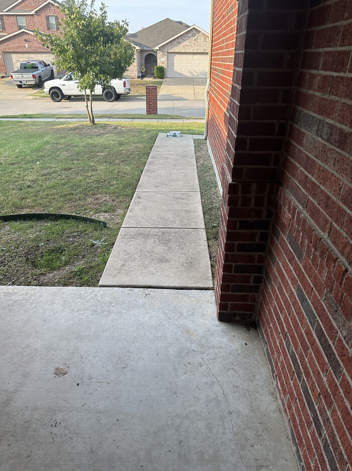 Package delivery left far from the door on sidewalk outside brick house in a residential neighborhood.