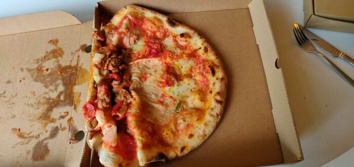 Partially eaten pizza with toppings pushed to one side in an open pizza box illustrating delivery gone off track.