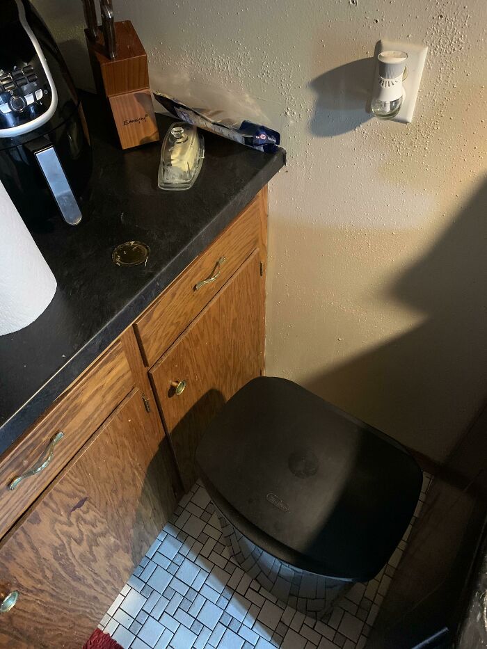 Small cramped kitchen corner with black trash can and wooden cabinets, illustrating toxic behavior in dads' home environments.