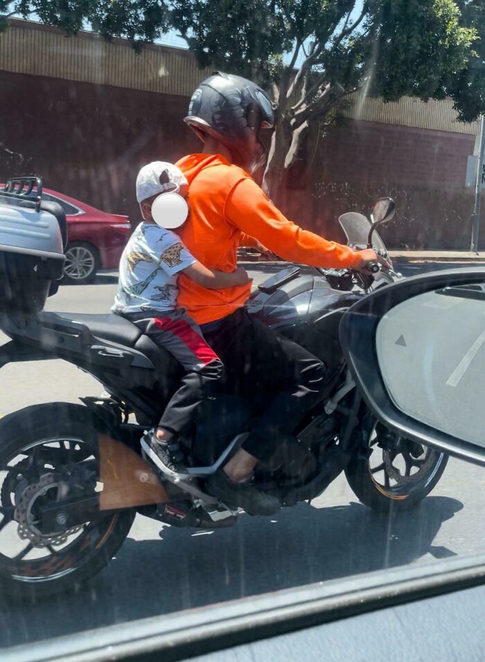 Man wearing helmet and orange hoodie riding motorcycle with child passenger, illustrating toxic dad behavior concerns.